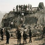 A group of people standing around rubble on top of a hill.