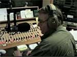A man wearing headphones and sitting at a mixing board.